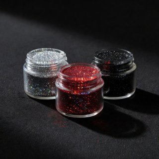 3D render of cosmetic glitter pots in silver, crimson and black arranged on a dark ground